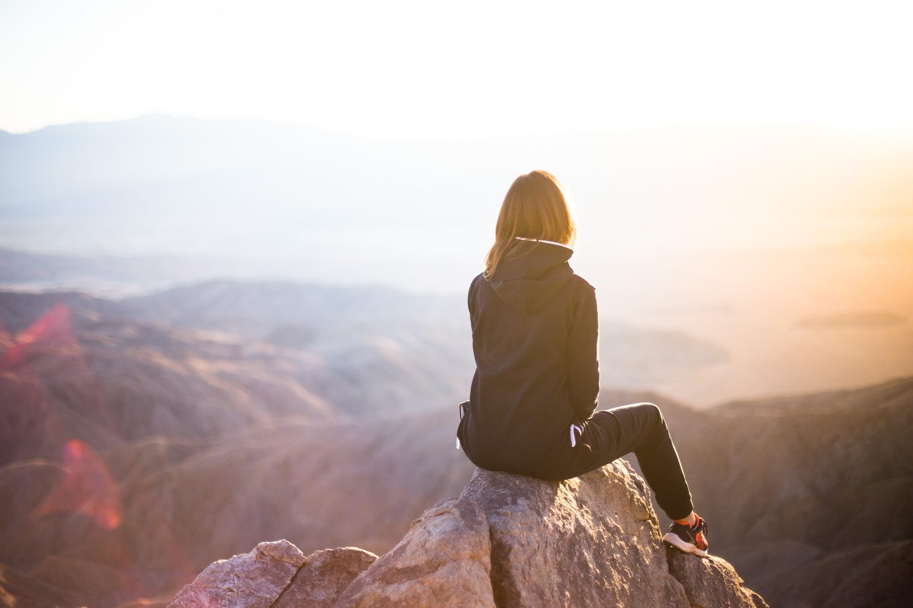 Someone sitting on a rock, looking out over hills at sunrise