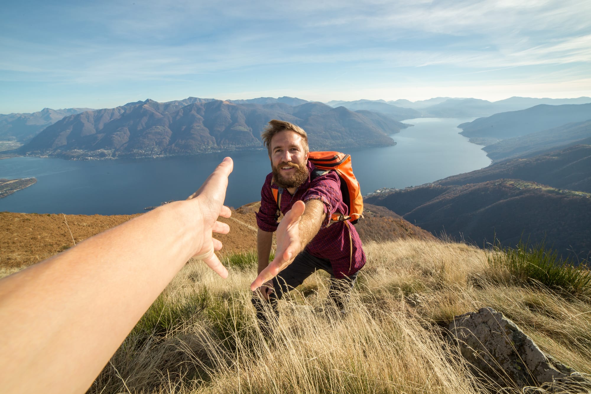 A hiker on a mountainside above a lake, reaching out to take a helping hand