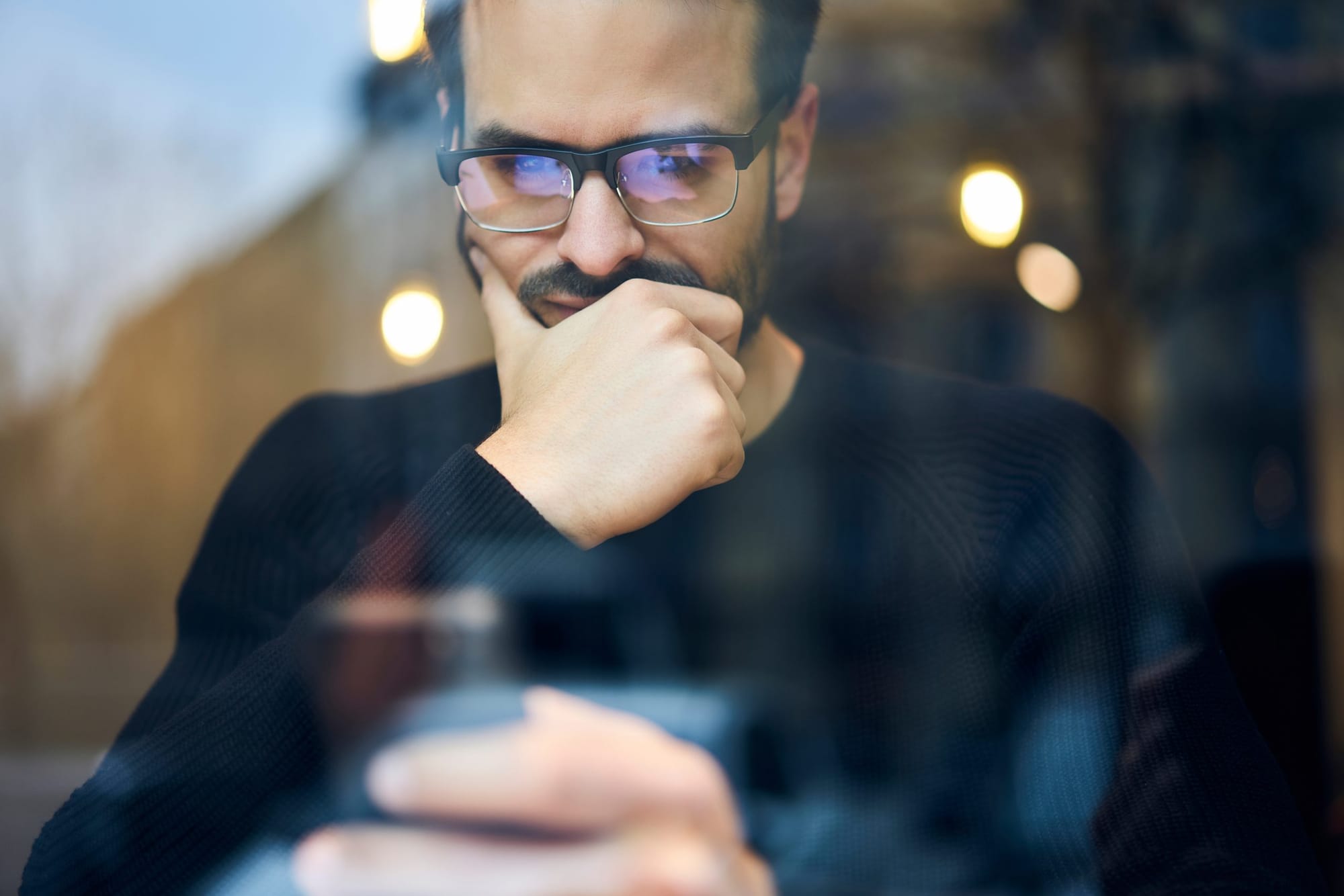 A man thinking, his hand at his chin, looking down at a phone